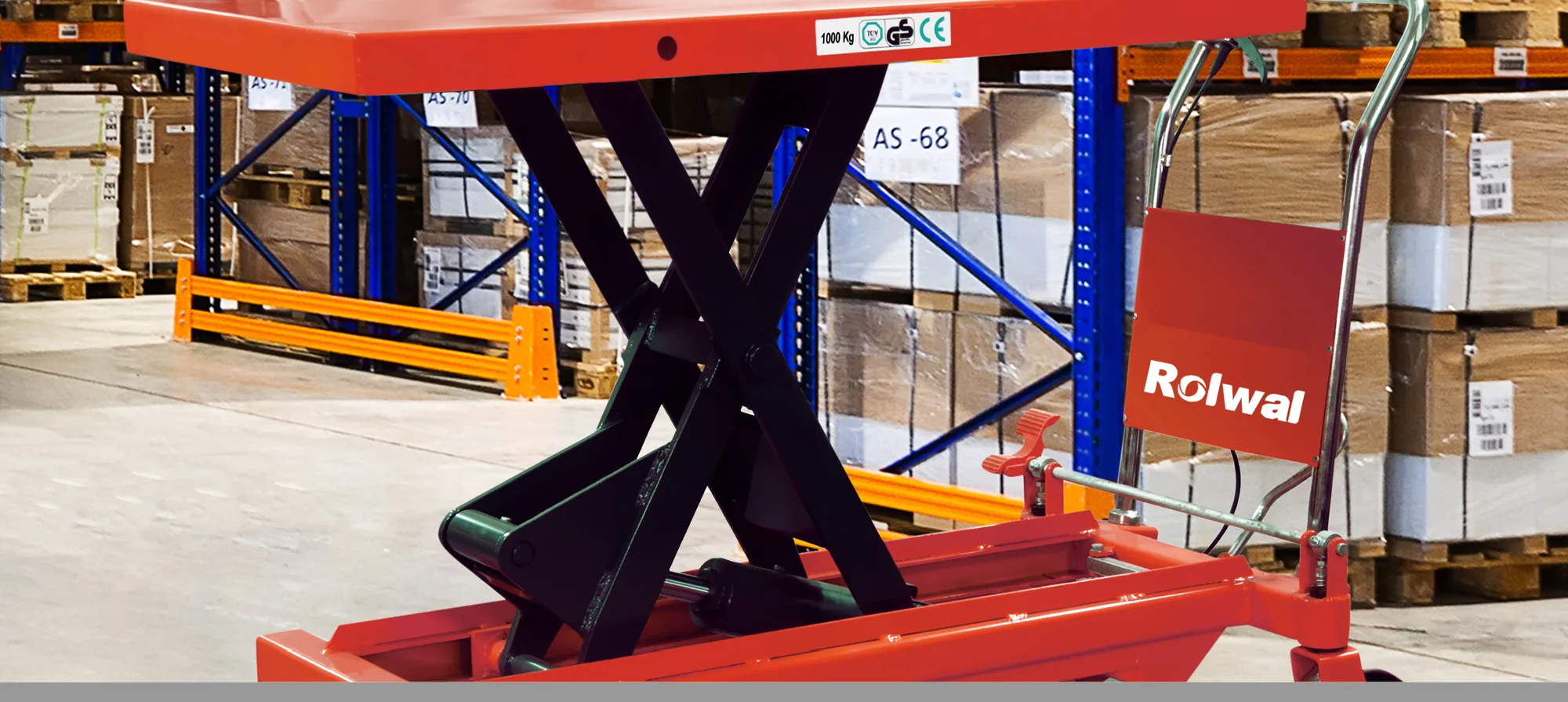 1 ton kapasiteli Rolwal makaslı yük platformu, palet rafları arasındaki koridorda tablası kaldırılmış halde